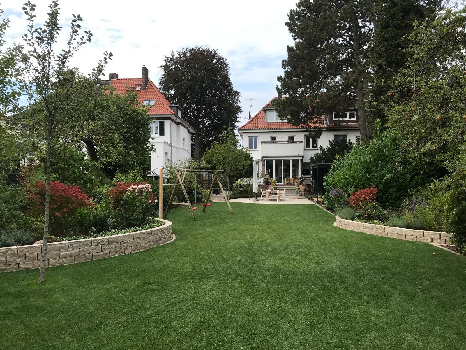 Angelegter Hausgarten mit großer Rasenfläche, Trockenmauern aus Naturstein, Staudenbeeten, einer Schaukel und der Terrasse am Haus