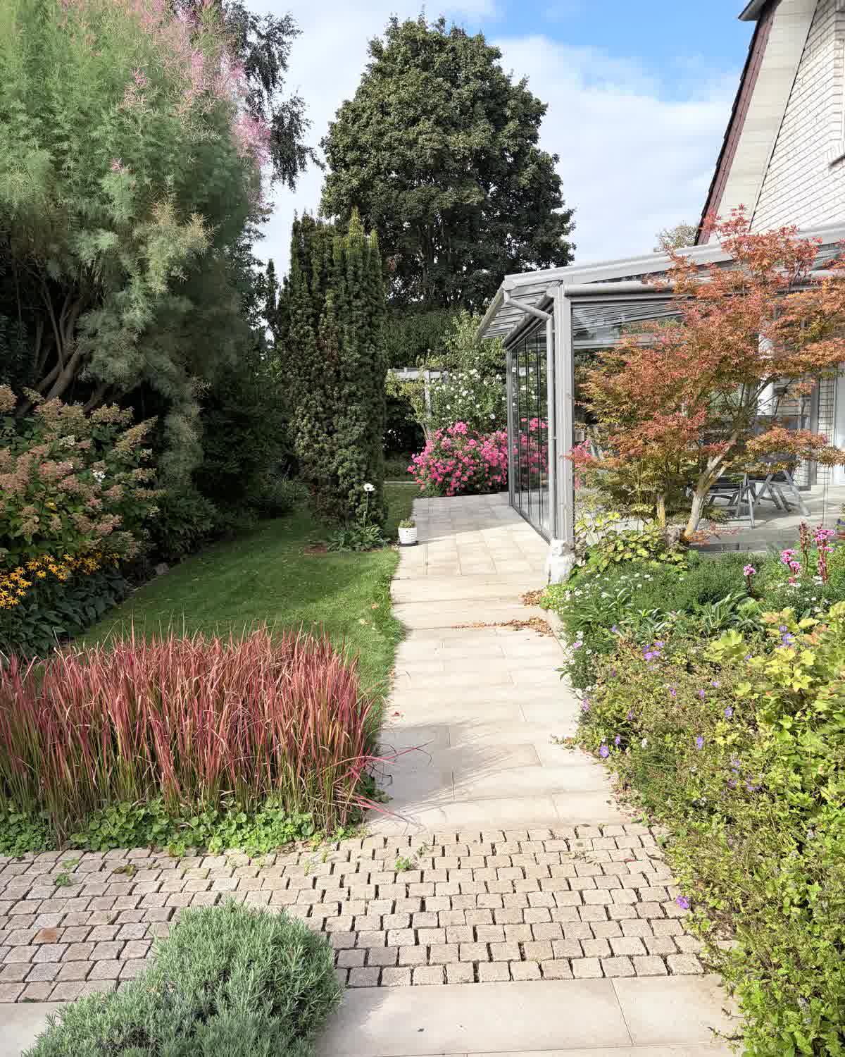 Fertiger Privatgarten mit Plattenweg, Stauden, Ziergräsern und Wintergarten