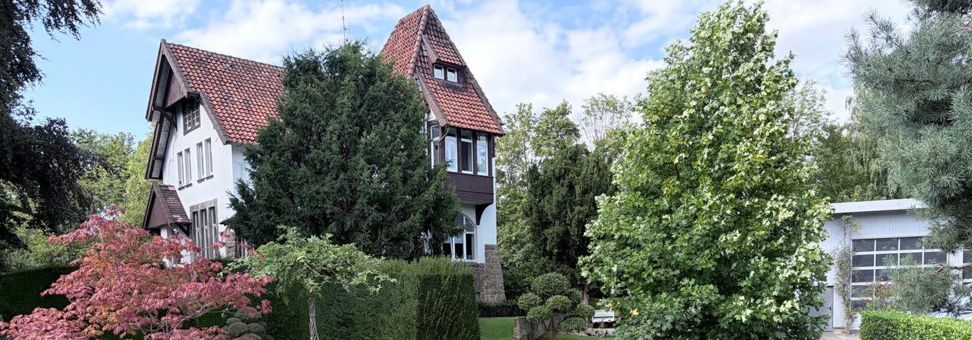 Die Jugendstilvilla des Betriebs an der Bemeroder Straße mit Rasen, geschnittenen Formgehölzen, Fächerahorn und der Halle rechts